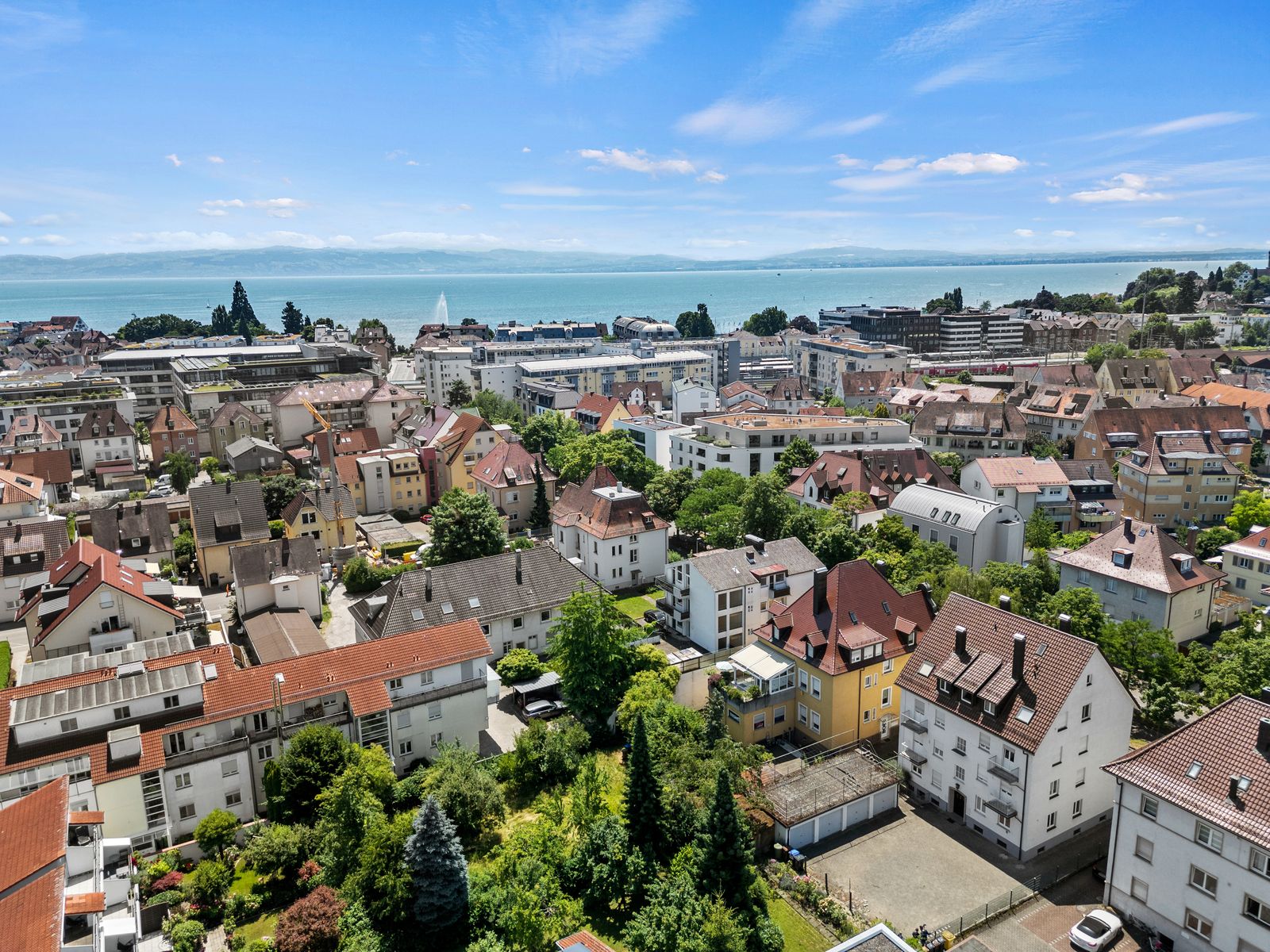 Luftbild von Friedrichshafen: Wohnhäuser mit Ziegeldächern, dahinter der Bodensee und die Schweizer Berge